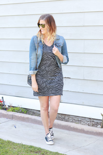 A Zebra Printed Dress featured by popular US Style Blogger, The Fashionista Momma; woman wearing a zebra print dress with converse and a denim jacket.